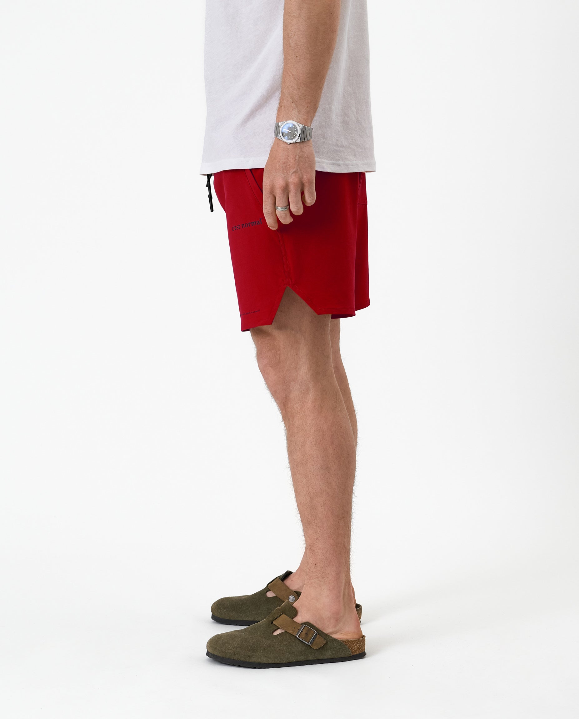 The Shorts in red — side view showing the notched hem and C'est normal logo