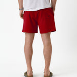 The Shorts in red — back view worn with a white t-shirt and olive sandals