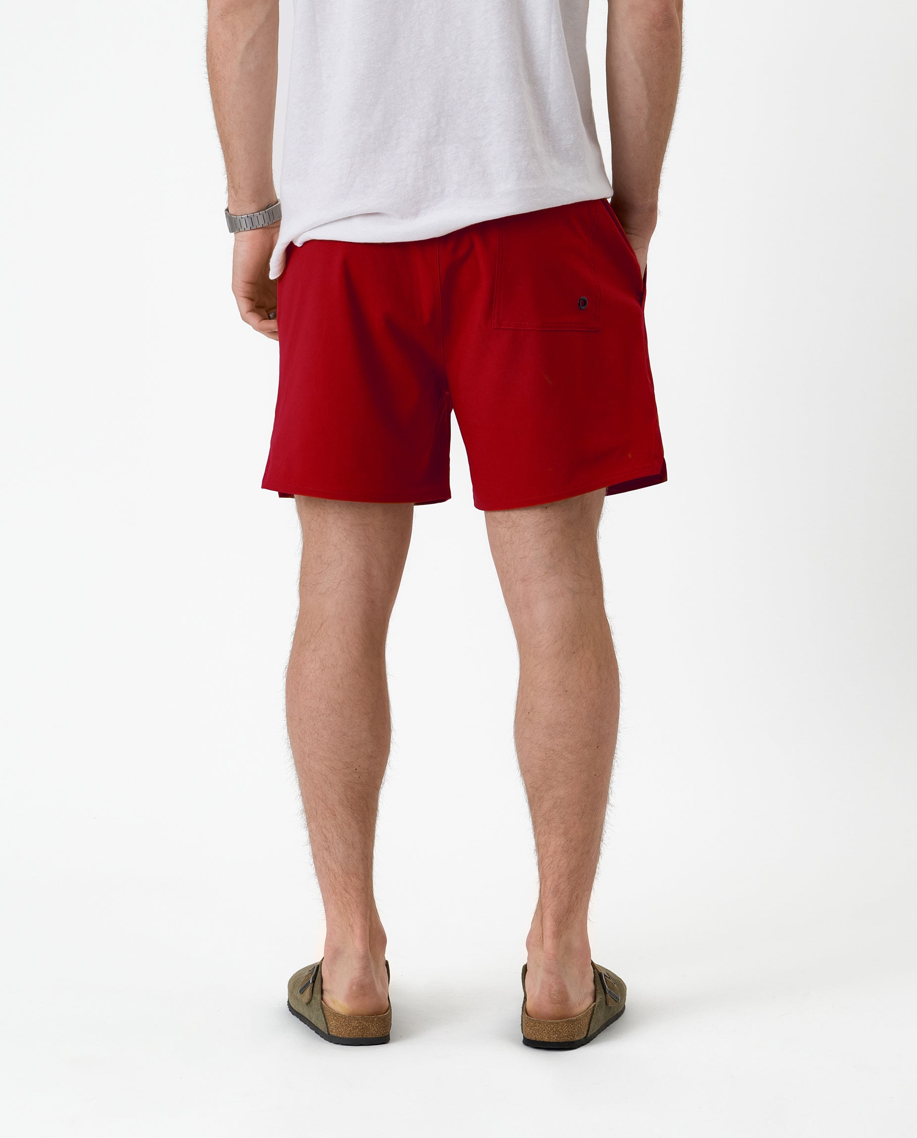 The Shorts in red — back view worn with a white t-shirt and olive sandals