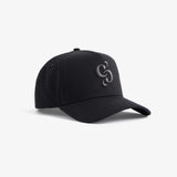 A front angled view of The Snapback Cap in black, resting on a white background. The image highlights the dark embroidered c'est normal mirror logo on the front panel.