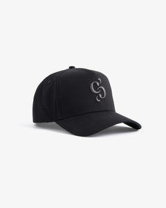 A front angled view of The Snapback Cap in black, resting on a white background. The image highlights the dark embroidered c'est normal mirror logo on the front panel.