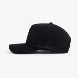 A side view of The Snapback Cap in black, placed on a white background. The image highlights the curved brim and the embroidered c'est normal text on the side panel.