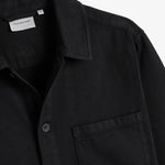 The Workwear Overshirt in black — close-up of the collar and chest pocket with subtle branding