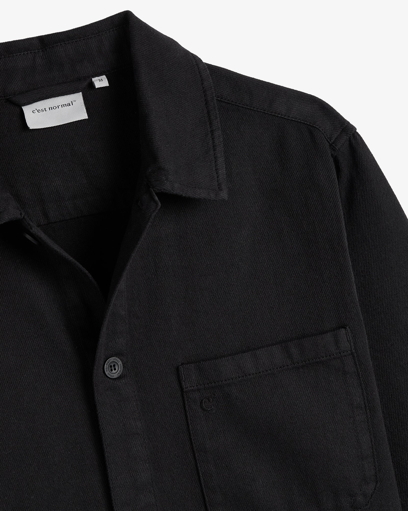 The Workwear Overshirt in black — close-up of the collar and chest pocket with subtle branding