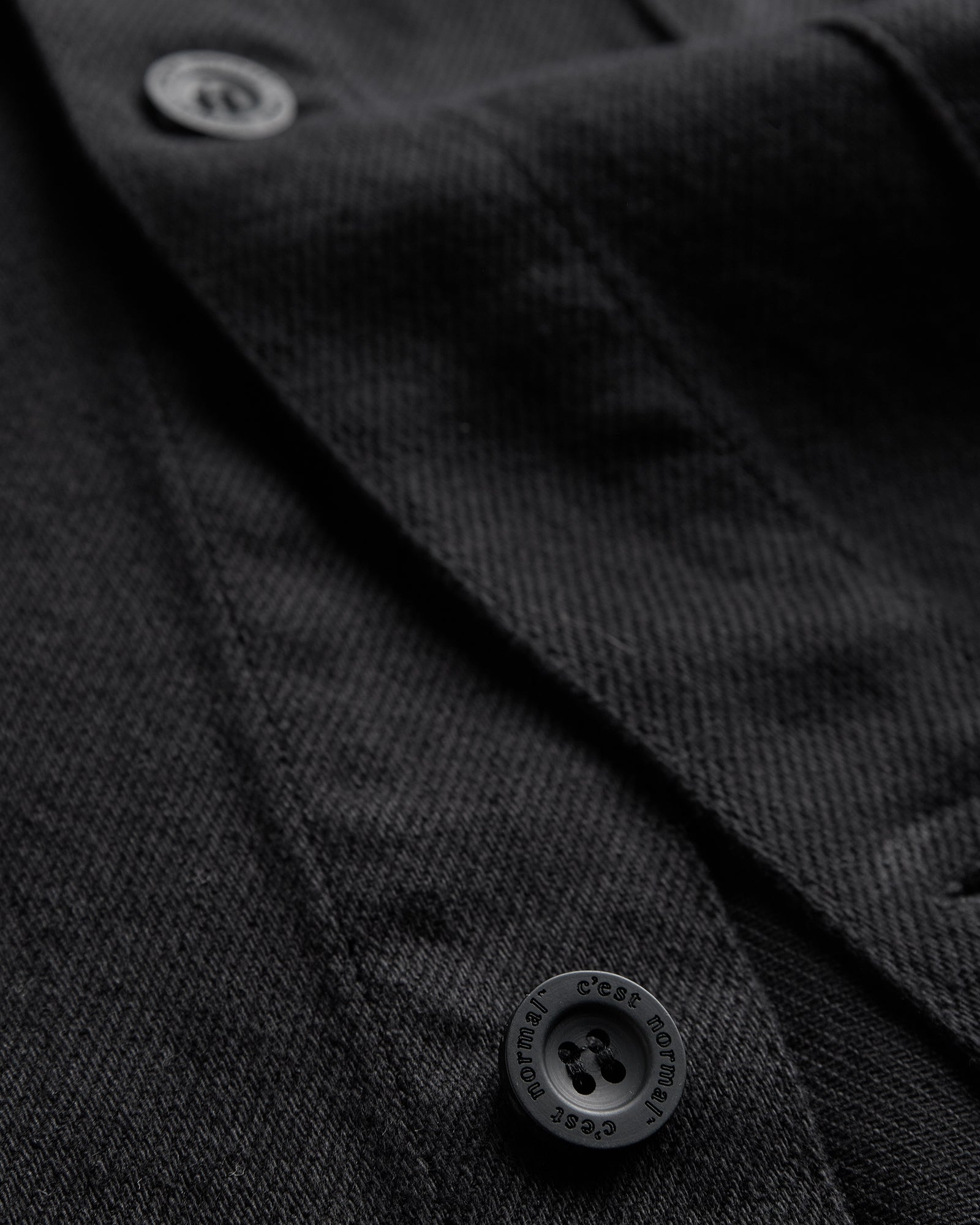 The Workwear Overshirt in black — close-up of the buttons engraved with C'est normal