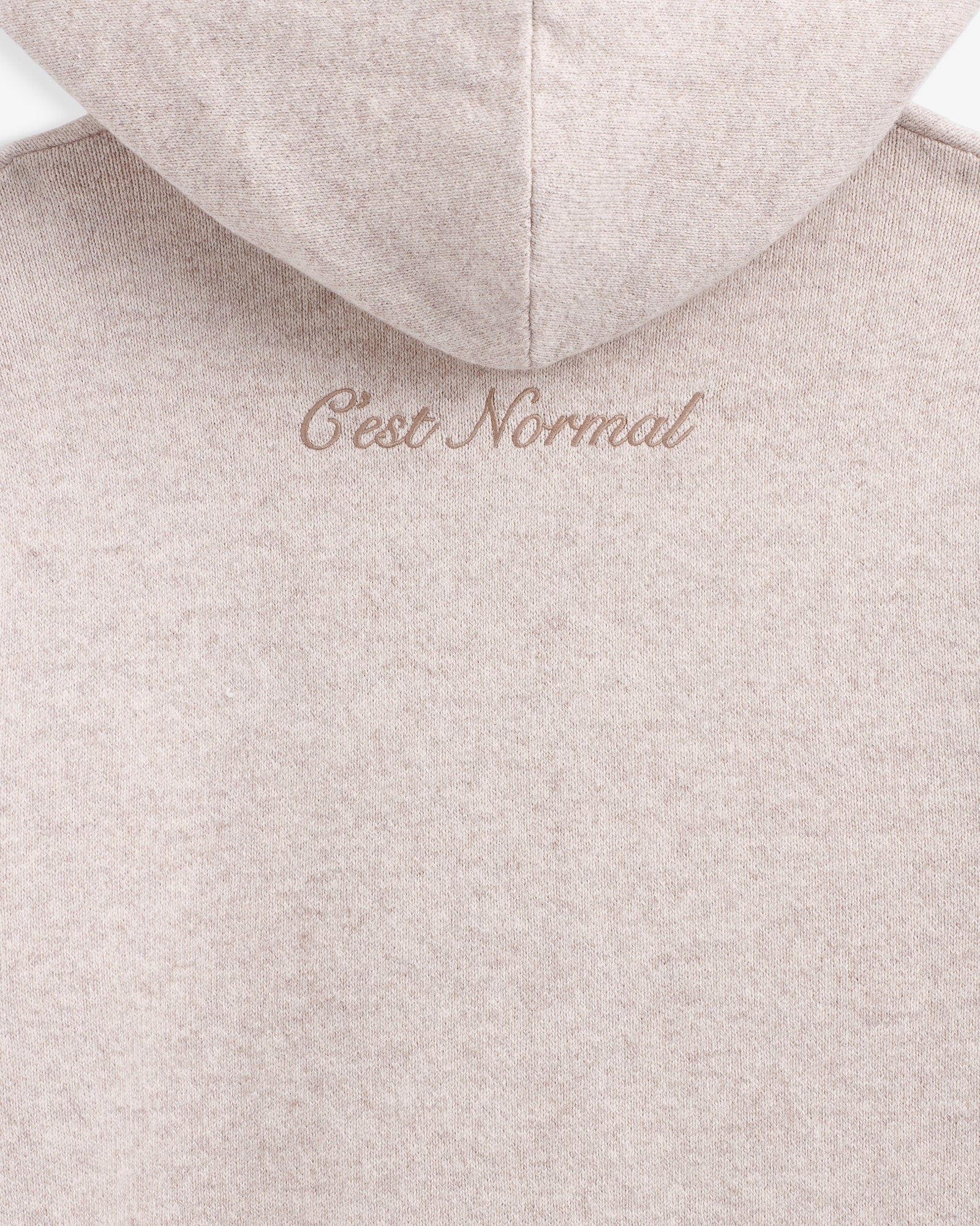 The Toulouse Hoodie in beige — close-up of embroidered C'est normal logo below the hood
