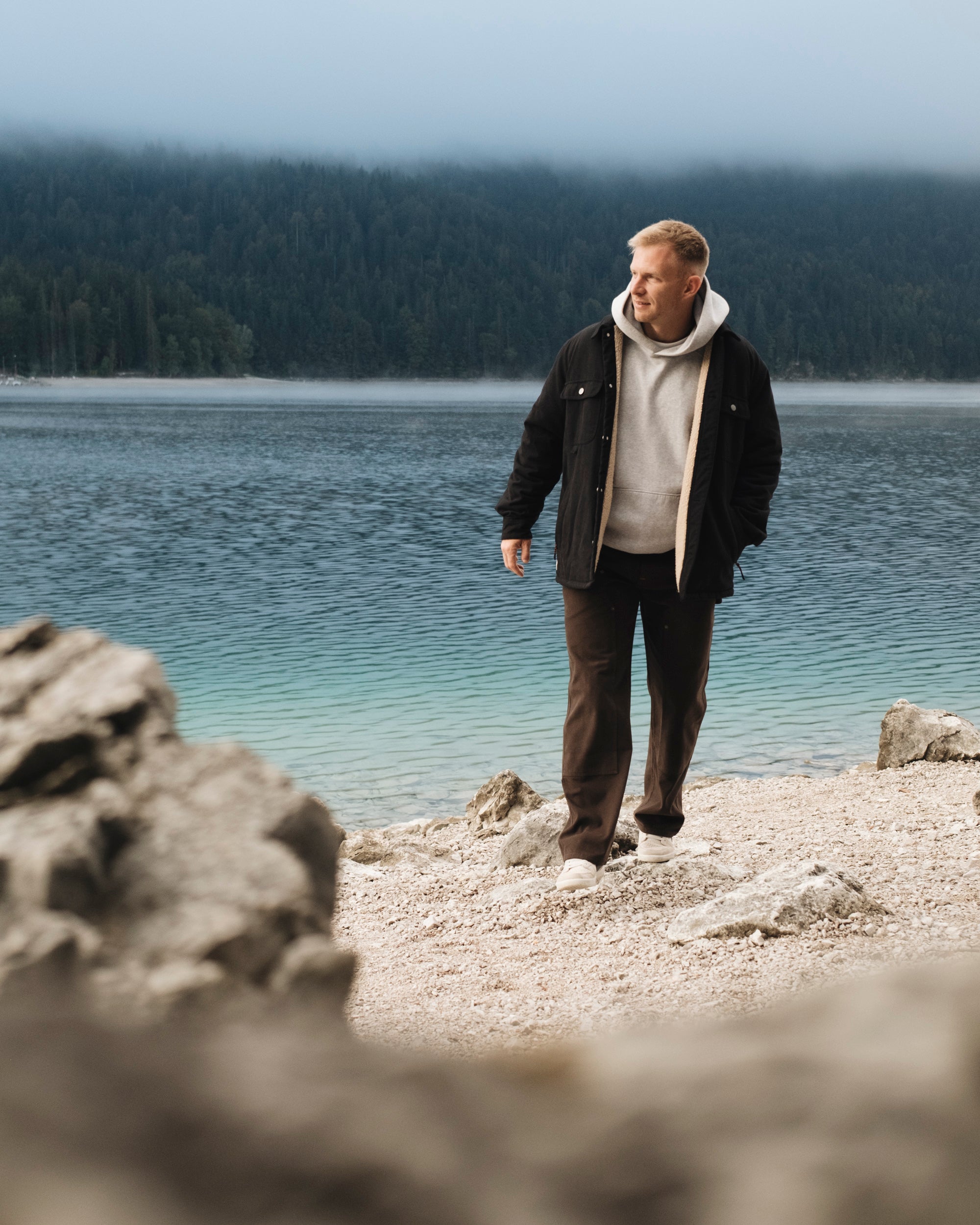 The Carpenter Pants in brown — worn by a man walking by a lake