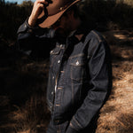 The Denim Jacket in dark indigo — worn outdoors with a brown hat