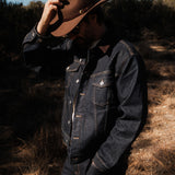 The Denim Jacket in dark indigo — worn outdoors with a brown hat