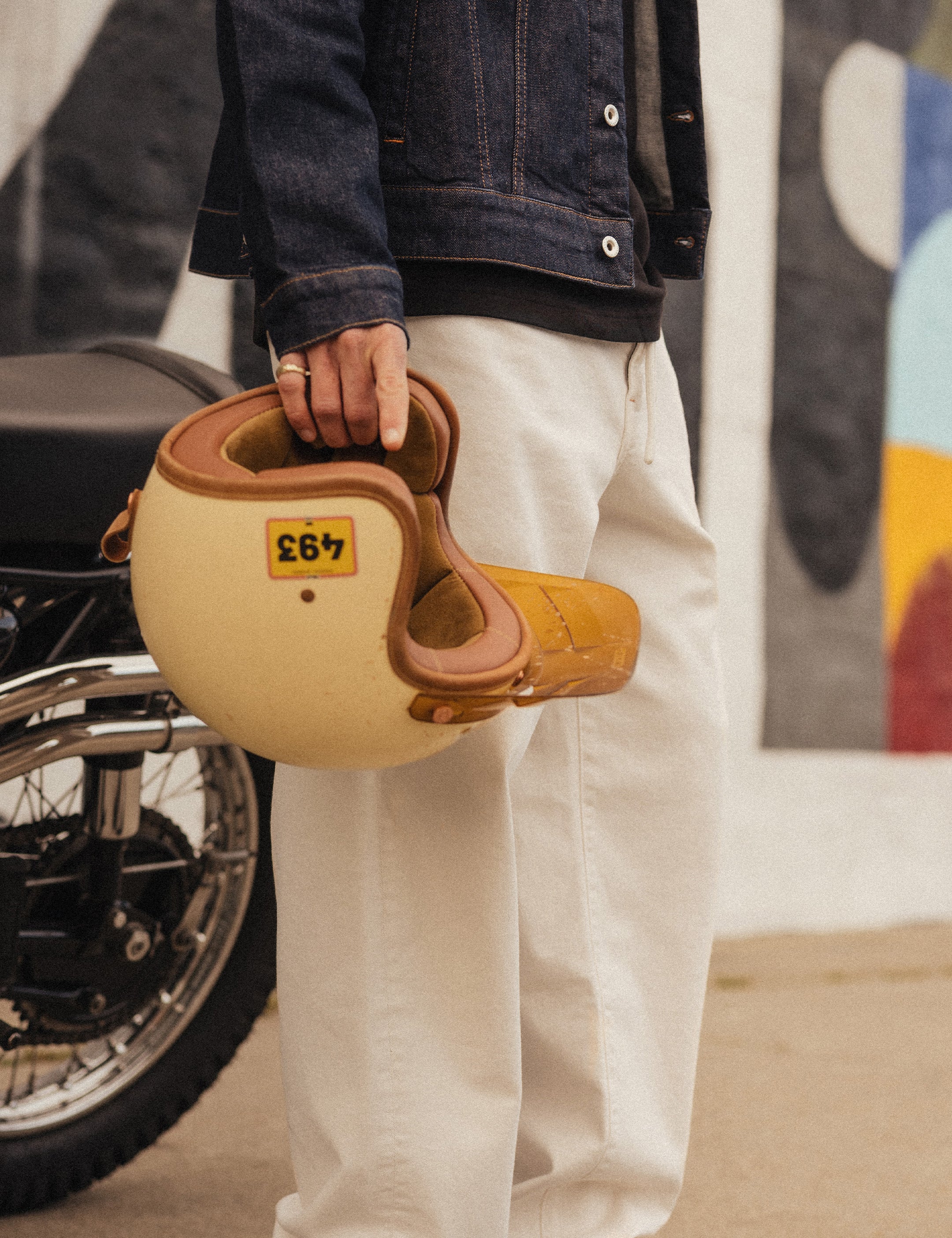 The Jeans Relaxed Straight Fit in ecru — worn while holding a motorcycle helmet