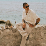 The Holiday Linen Trouser in Natural — sitting on a stone wall next to a chessboard