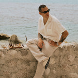 The Holiday Linen Trouser in Natural — sitting on a stone wall next to a chessboard