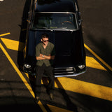The Holiday Linen SS Shirt in dark khaki — worn while leaning against a vintage black car