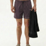 A model wearing The Shorts in Dark Boulevard, standing against a white background while holding a black towel. The shorts feature an elasticated waistband with a drawstring, side pockets, and the white c'est normal logo on the leg.