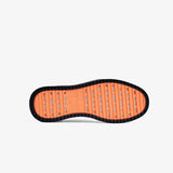 A bottom view of The Sneakers 2.0 in black, laid flat on a white background. The image highlights the original orange EVA rubber grid sole featuring the c'est normal logo.