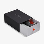 The Sneakers 2.0 in grey, partially pulled out of a black and white sliding shoebox on a white background. The black outer sleeve features the white c'est normal logo, and the inner white drawer has a bright orange pull tab.