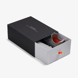 The Sneakers 2.0 in grey, partially pulled out of a black and white sliding shoebox on a white background. The black outer sleeve features the white c'est normal logo, and the inner white drawer has a bright orange pull tab.
