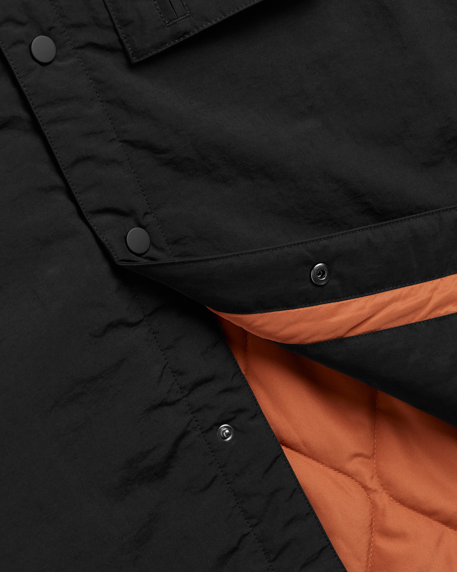 The Utility Vest in black — close-up showing the orange quilted lining and snap buttons